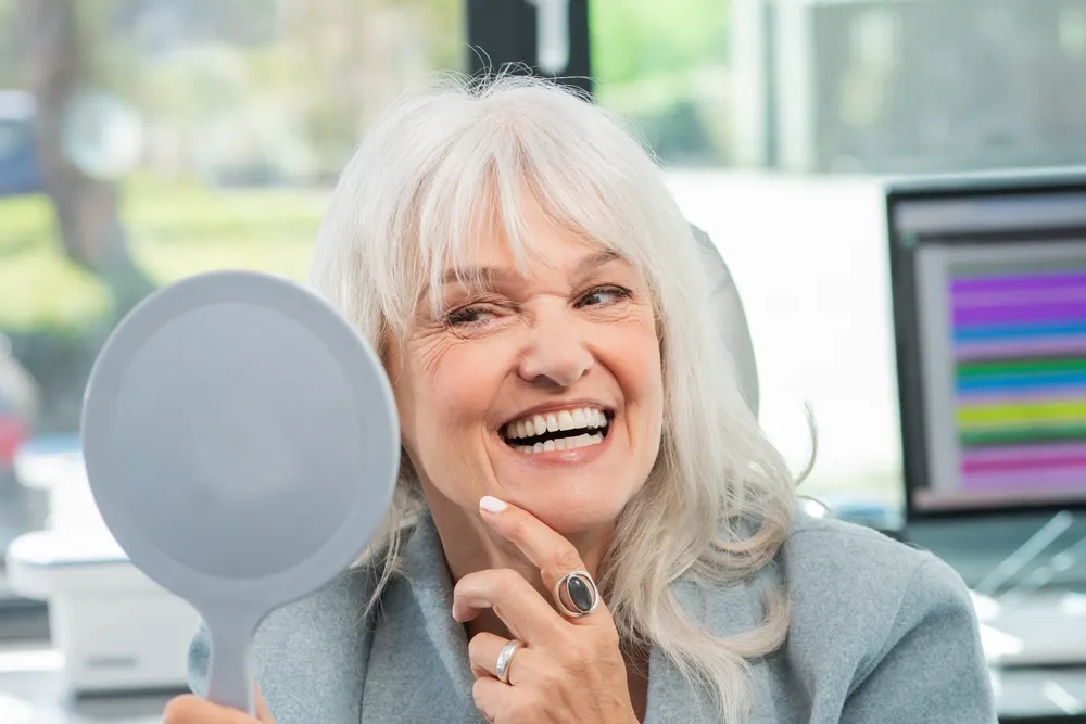 Lachende vrouw bekijkt haar nieuwe gebit in de spiegel